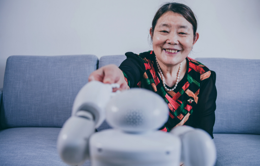 An elderly woman is smiling and shaking hands with a robot