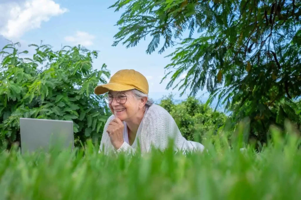 Woman with hat and glasses lying on lawn using laptop
and smiling