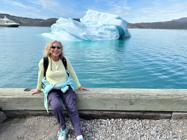 Margie Goldsmith poses in front of an iceberg in Greenland.